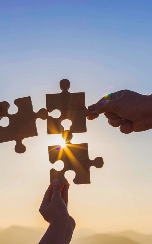 Human hands holding jigsaw puzzle at sunset background.team work and success and strategy concept.